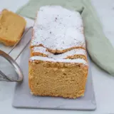 Puszyste ciasto keto, posypane cukrem pudrem, z dwoma kawałkami obok. Obok sitko do cukru.