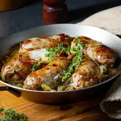 Pieczona biała kiełbasa surowa z cebulą i tymiankiem w metalowej patelni.