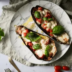 Dwa połówki bakłażana pieczonego z pomidorkami i mozzarellą, udekorowane listkami bazylii.