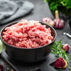 Mielone inaczej: świeże mięso mielone w misce, czosnek, rozmaryn i przyprawy na ciemnym tle.
