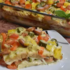 Zapiekanka z tostów z parówkami, pomidorami, ogórkiem i serem w naczyniu żaroodpornym.