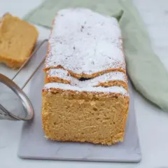 Puszyste ciasto keto, posypane cukrem pudrem, z dwoma kawałkami obok. Obok sitko do cukru.