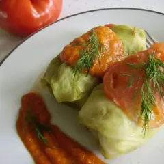 Gołąbki z pysznym farszem, polane sosem pomidorowym i udekorowane koperkiem. Obok leży pomidor.