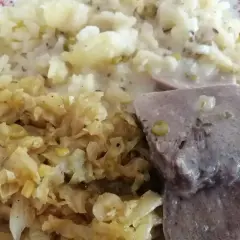 Na talerzu ułożone są plastry gotowanych ozorków w sosie, obok porcja ziemniaków i duszona kapusta.