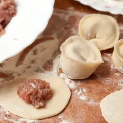 Przygotowanie pierogów: na okrągłym cieście leży farsz na pierogi z mięsem mielonym, obok uformowane pierogi.
