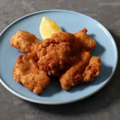 Chrupiące kawałki karaage, złociste i apetyczne, podane z ćwiartką cytryny na niebieskim talerzu.