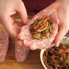 Ręce formują zrazy z mięsa mielonego, nadziewając je farszem z warzyw. Obok leżą gotowe, owalne kotleciki.