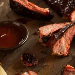 Soczyste żeberka BBQ, polane sosem, obok miseczka z marynatą do żeberek i pędzelek.