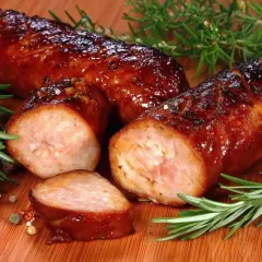 Soczysta kiełbasa z piekarnika, rumiana i aromatyczna, z gałązkami rozmarynu i ziarnami pieprzu na desce.