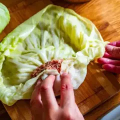 Ręce zwijają liść kapusty z farszem mięsnym. To początek przygotowań do pysznego dania, idealnego na przepis na gołąbki na 1kg mięsa.
