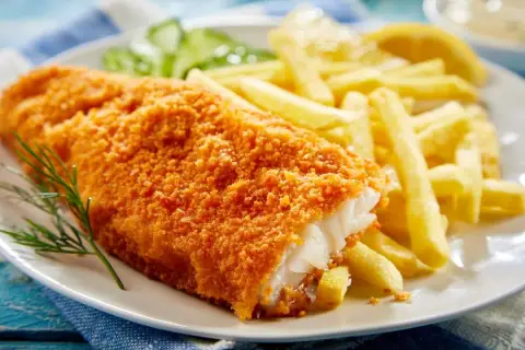 Chrupiący filet po parysku z frytkami i cytryną, ozdobiony gałązką koperku.