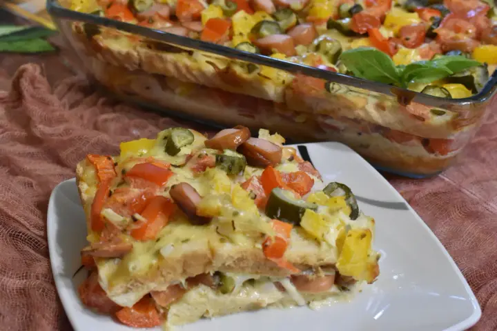 Zapiekanka z tostów z parówkami, pomidorami, ogórkiem i serem w naczyniu żaroodpornym.