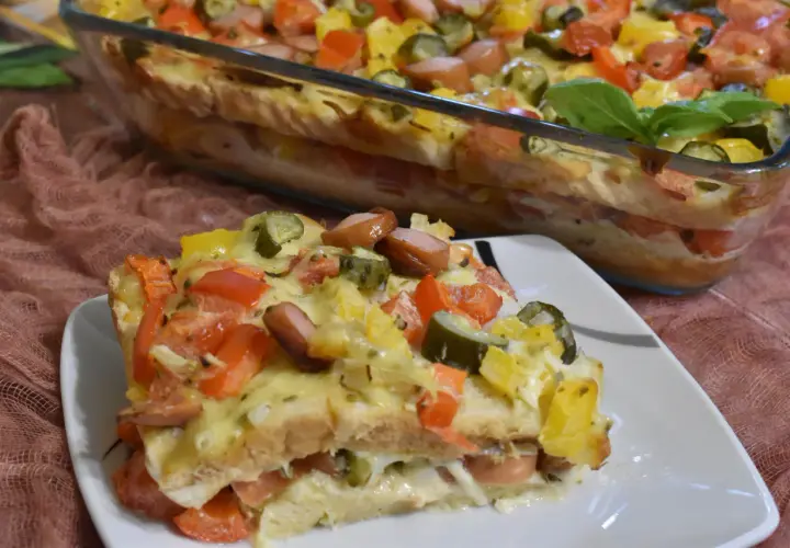 Zapiekanka z tostów z parówkami, pomidorami, ogórkiem i serem w naczyniu żaroodpornym.