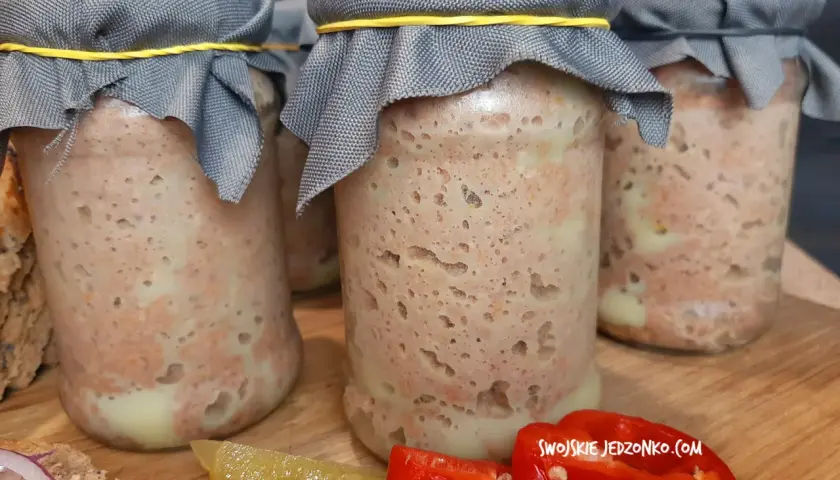 Słoiki z domowym pasztetem, przygotowanym według starego przepisu. Obok plasterki ogórka i papryki.