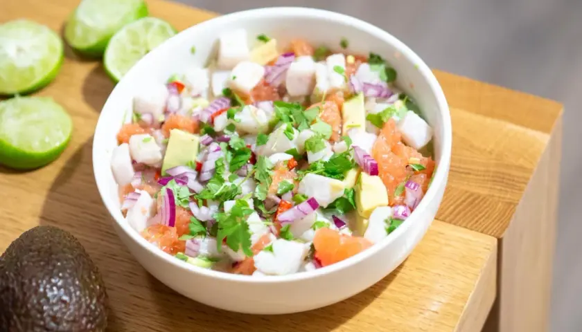 Pyszne ceviche z kawałkami ryby, awokado, grejpfruta, czerwonej cebuli i kolendry, podane w białej misce.