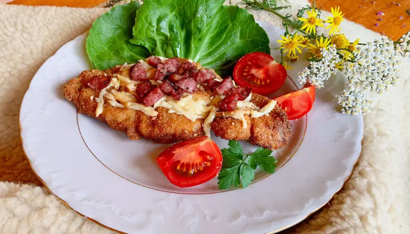 Schab po góralsku, panierowany kotlet z serem i boczkiem, podany z pomidorami i sałatą.