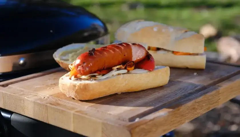 Pyszna kiełbasa z grilla w bułce z warzywami, gotowa do jedzenia na świeżym powietrzu.