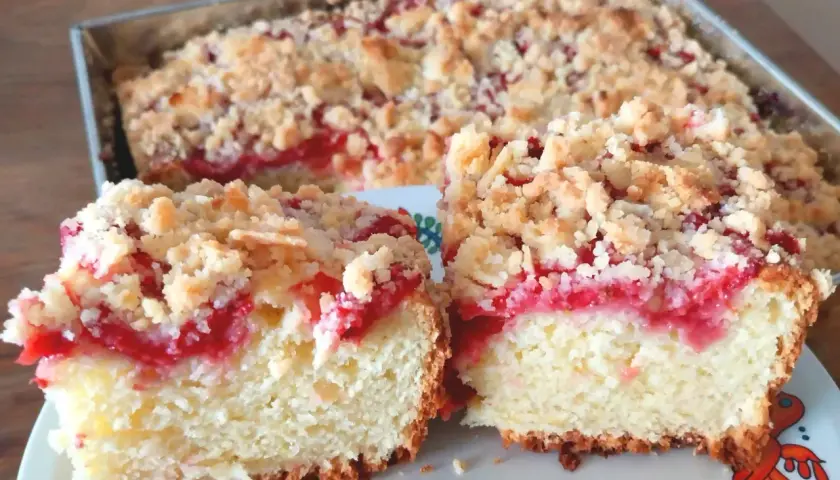 Puszysta babka z truskawkami i kruszonką, pokrojona na dwa kawałki, prezentuje się apetycznie.