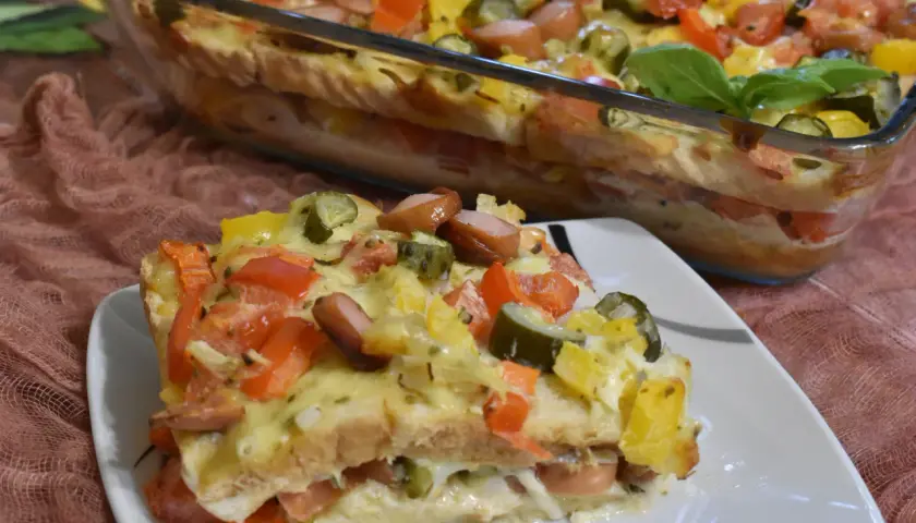 Zapiekanka z tostów z parówkami, pomidorami, ogórkiem i serem w naczyniu żaroodpornym.
