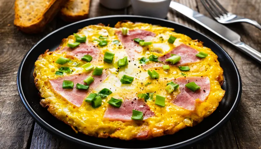 Pyszny omlet z szynką i serem, posypany szczypiorkiem, idealny na śniadanie. Dowiedz się, jak zrobić omlet z szynką i serem.