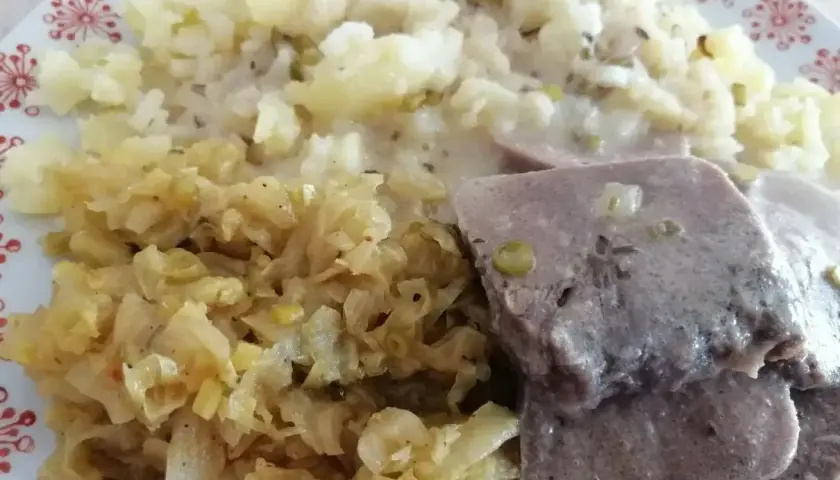 Na talerzu ułożone są plastry gotowanych ozorków w sosie, obok porcja ziemniaków i duszona kapusta.