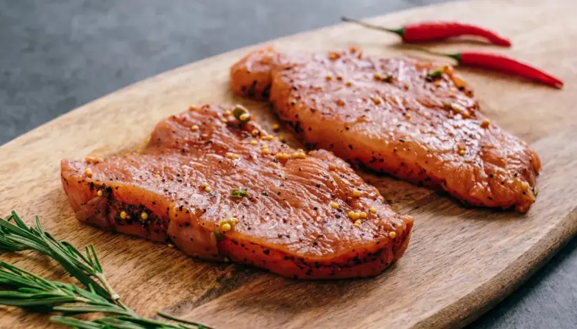 Dwa kawałki indyka w marynacie z gorczycą i pieprzem, obok gałązka rozmarynu i dwa czerwone chili.