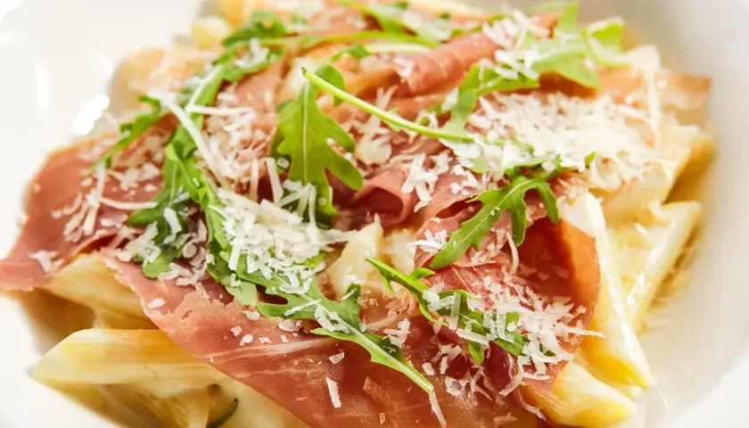 Penne z kremowym sosem, szynką parmeńską, rukolą i parmezanem. Pyszne danie, które zachwyci każdego smakosza.