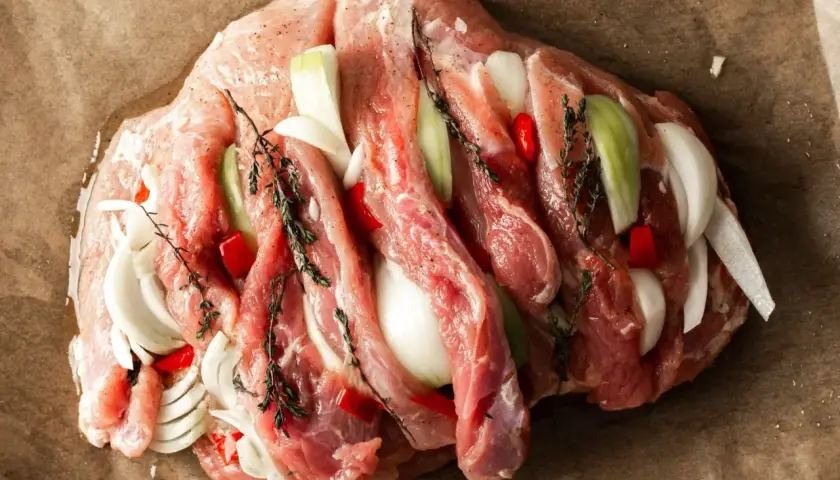 Przygotowanie dania z szynki wieprzowej na obiad: surowa szynka faszerowana cebulą, papryczką chili i ziołami na papierze do pieczenia.