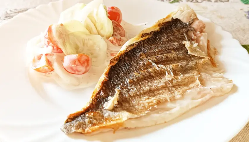 Dorada z grilla z chrupiącą skórką, podana z sałatką z pomidorków i ogórka w kremowym sosie.