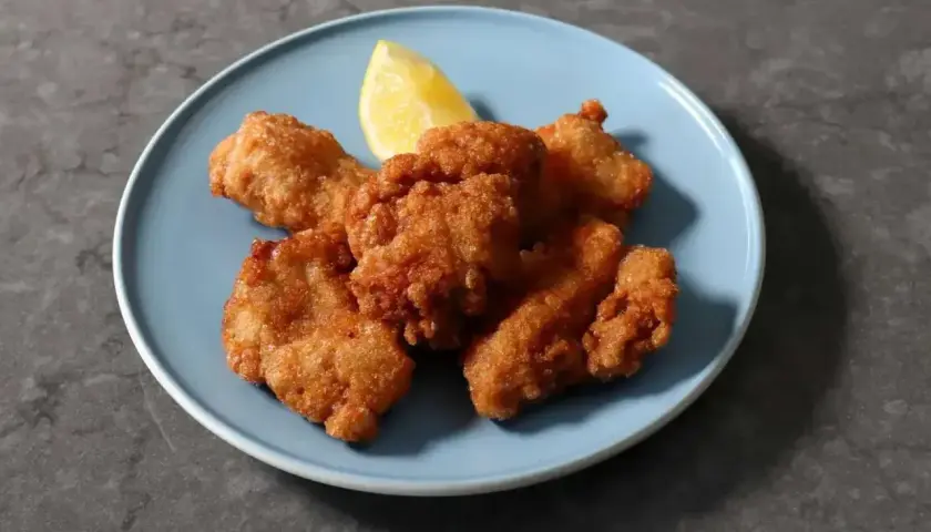 Chrupiące kawałki karaage, złociste i apetyczne, podane z ćwiartką cytryny na niebieskim talerzu.