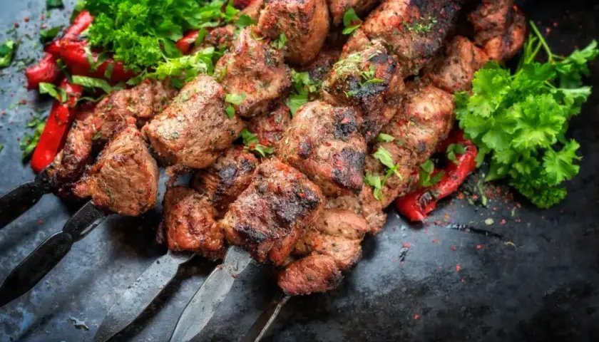 Soczyste kawałki kofta kebab na metalowych szpikulcach, ozdobione papryką i natką pietruszki.