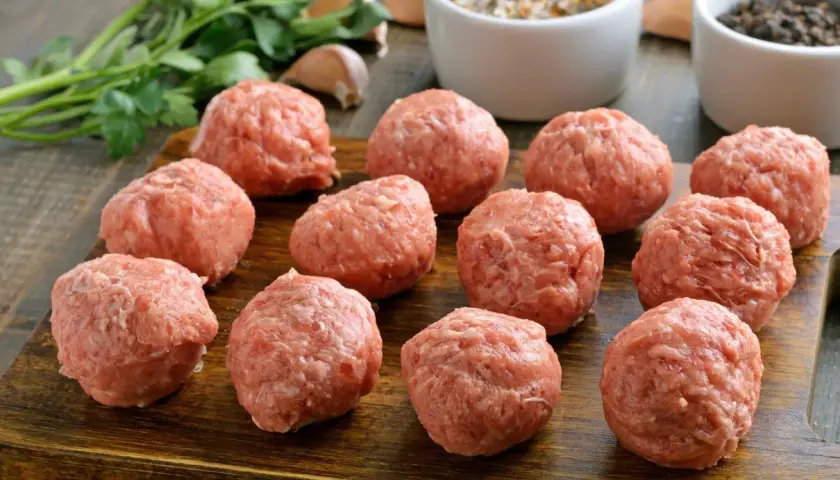 Surowe kotlety mielone gotowe do smażenia, obok przyprawy i zielenina. Idealny przepis na kotlety mielone z dodatkami.