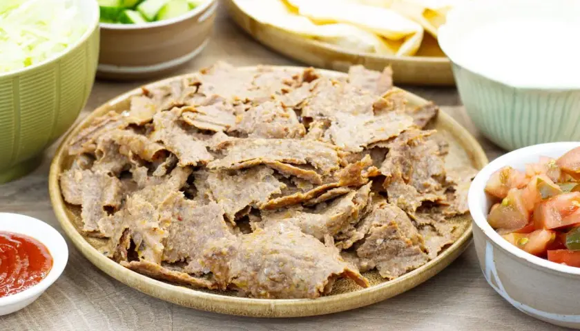 Pyszny kebab z piekarnika na talerzu, otoczony świeżymi warzywami, sosem i plackami. Idealny na domowy obiad.