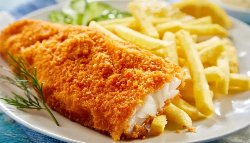 Chrupiący filet po parysku z frytkami i cytryną, ozdobiony gałązką koperku.