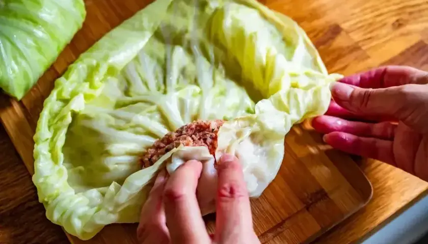 Ręce zwijają liść kapusty z farszem mięsnym. To początek przygotowań do pysznego dania, idealnego na przepis na gołąbki na 1kg mięsa.