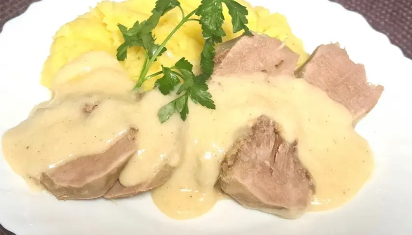 Kawałki ozorków w kremowym sosie chrzanowym, podane z purée ziemniaczanym i gałązką natki pietruszki.