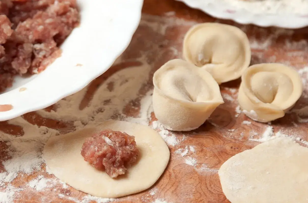 Przygotowanie pierogów: na okrągłym cieście leży farsz na pierogi z mięsem mielonym, obok uformowane pierogi.