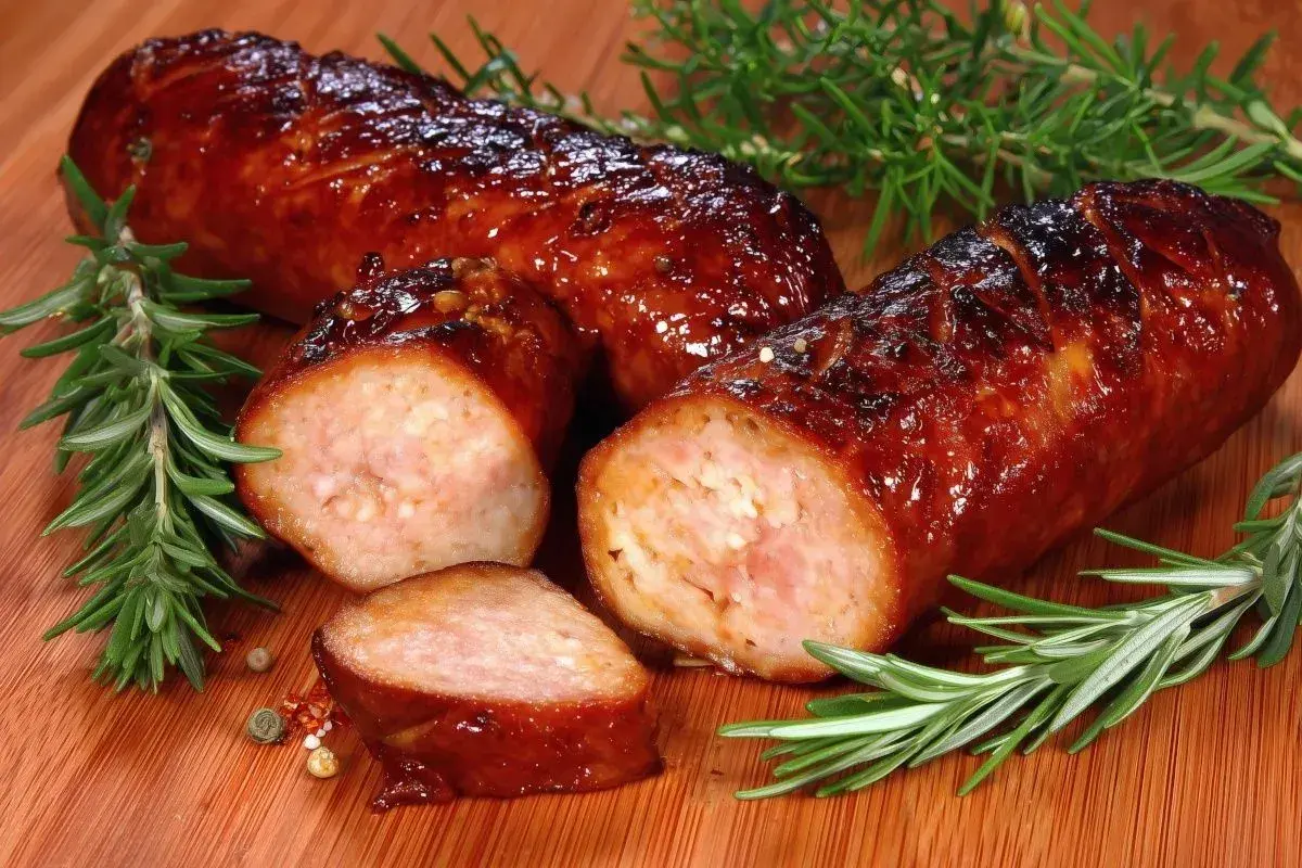 Soczysta kiełbasa z piekarnika, rumiana i aromatyczna, z gałązkami rozmarynu i ziarnami pieprzu na desce.