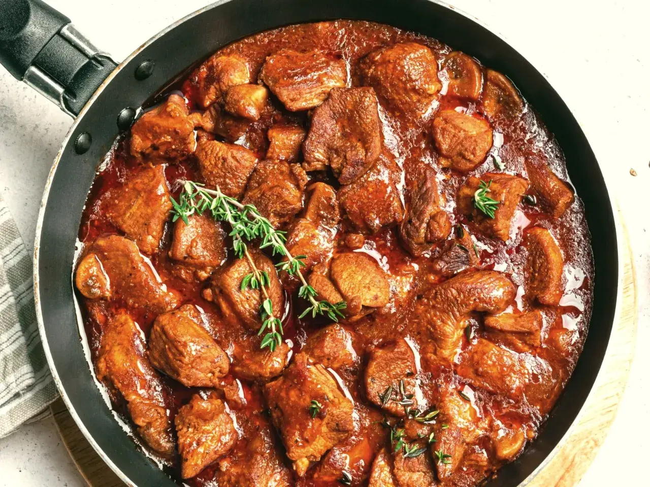 Gicz wołowa duszona w gęstym sosie, ozdobiona gałązkami tymianku, kusi aromatem i apetycznym wyglądem.