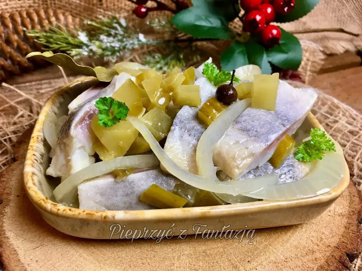 Jak zrobić dobre śledzie po wiejsku? Aromatyczne śledzie z cebulą, ogórkiem i jabłkiem, udekorowane natką pietruszki.