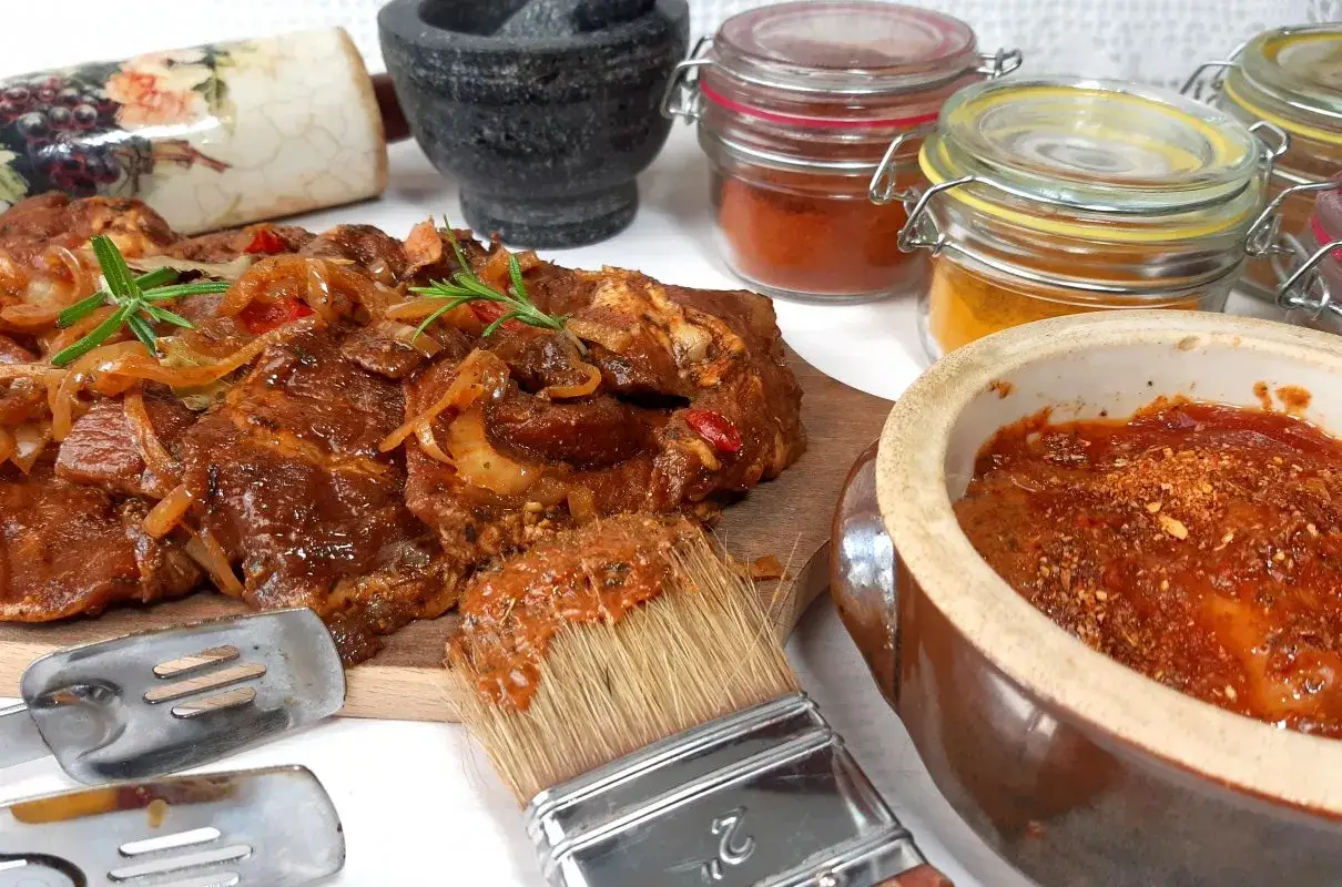 Karkówka w aromatycznej marynacie, gotowa do pieczenia. Obok pędzel z marynatą, przyprawy i kamienny moździerz.