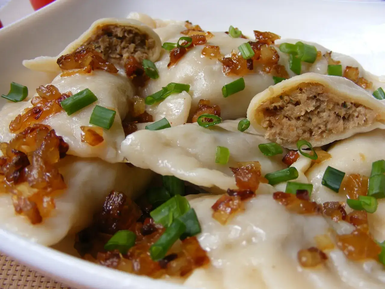 Pyszne pierogi z farszem na pierogi z mięsem mielonym, posypane skwarkami i szczypiorkiem.