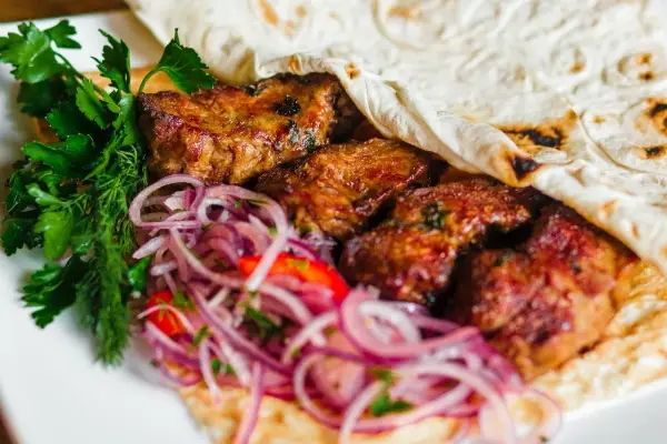 Soczyste mięso kebab zawinięte w placek, podane z czerwoną cebulą i świeżą natką pietruszki.