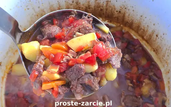 Gulasz z kociołka żeliwnego na ognisku, pełen mięsa, ziemniaków i warzyw, paruje apetycznie.